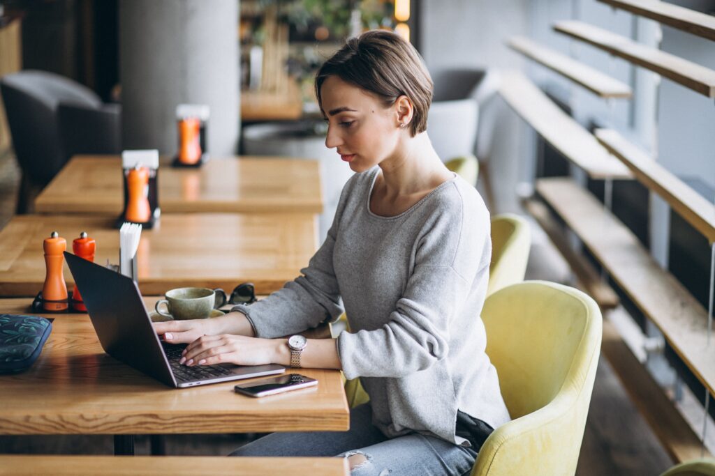 woman-sitting-cafe-drinking-coffee-working-computer-min